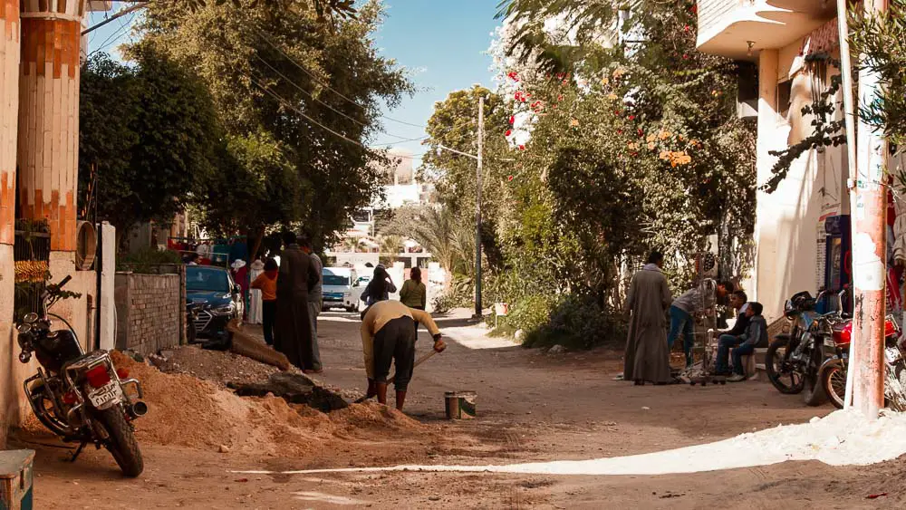 Straße im Zentrum von Luxor mit einem Motorrad, Menschen und Bäumen. 