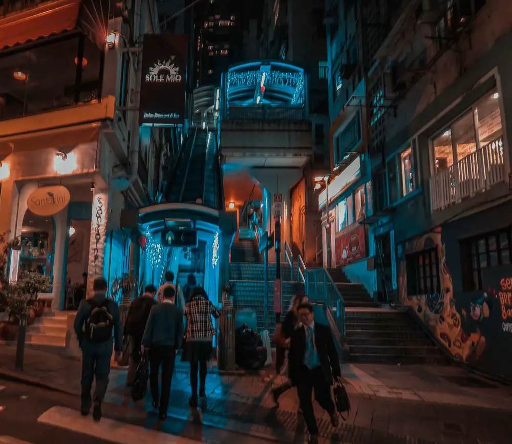 Midlevel Escalators in der Nacht mit Bars, beleuchtet in orangen und blauen Lichtern. 