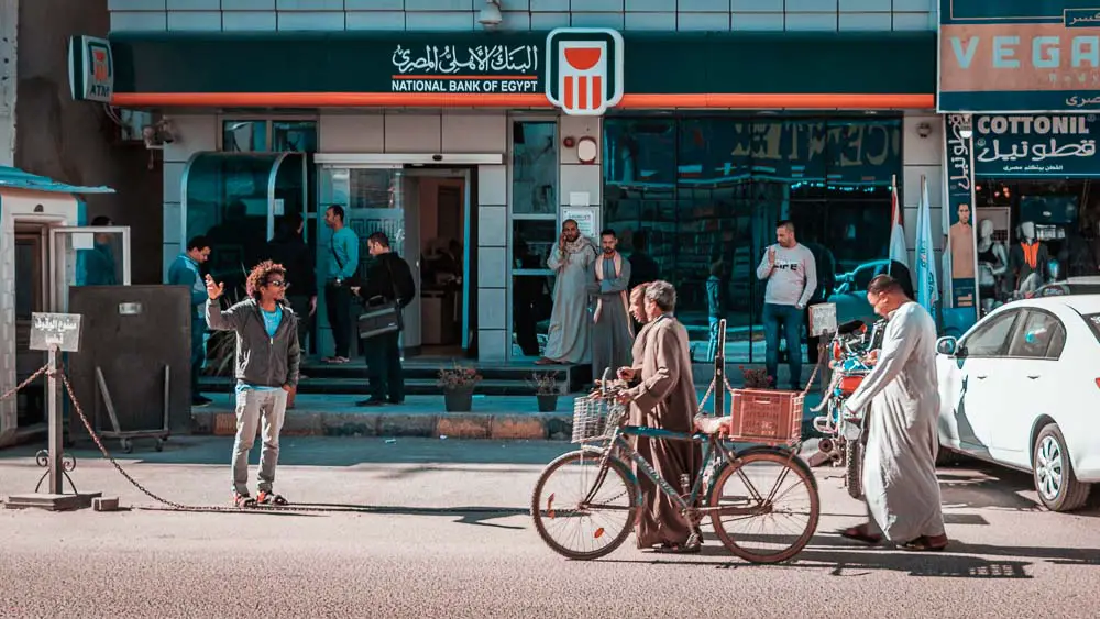 Filiale der National Bank of Egypt in der Innenstadt von Hurghada mit Autos, Menschen ud einem Wachposten davor. 