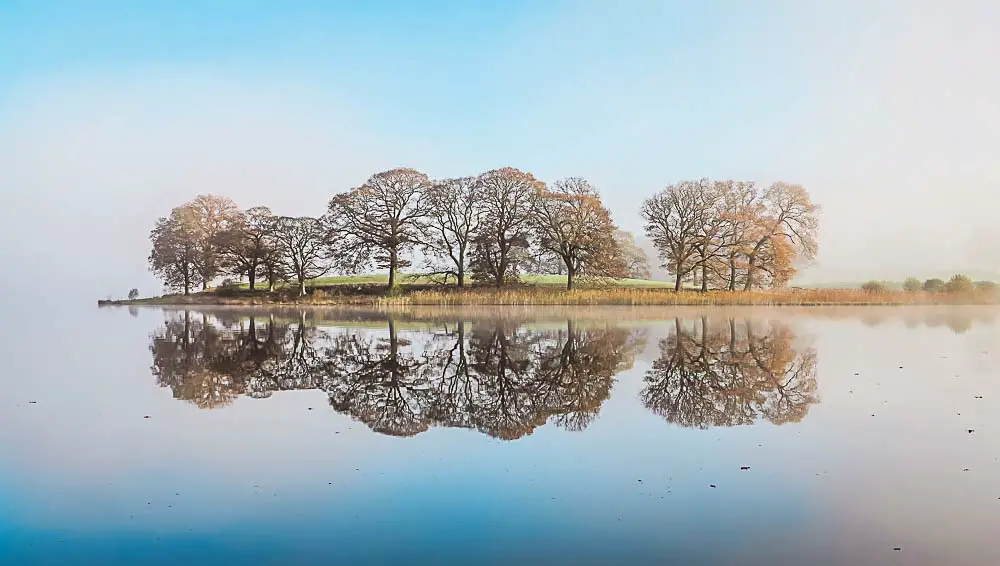 Bild von einem See mit Nebel im Lake District National Park mit Bäumen auf einer kleinen Insel