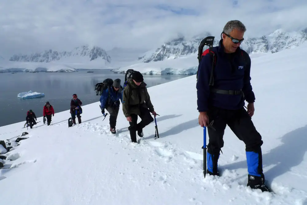 Bergsteiger auf einer Schneelandschaft in der Antarktis mit Blick auf das Meer Bergsteiger auf einer Schneelandschaft in der Antarktis mit Blick auf das Meer
